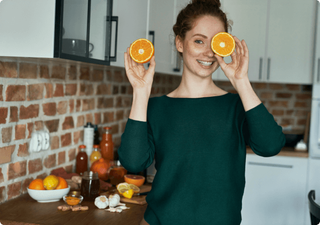 vrouw staat glimlachend in de keuken, met een halve sinasappel voor haar gezicht