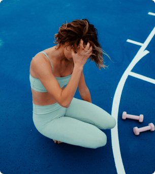 vrouw zit gehurkt op de grond met 2 dumbels naast haar op de grond