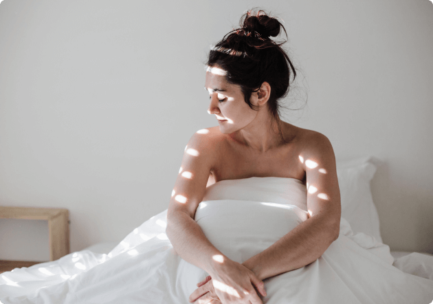 vrouw zit rechtop in bed de zon val op haar
