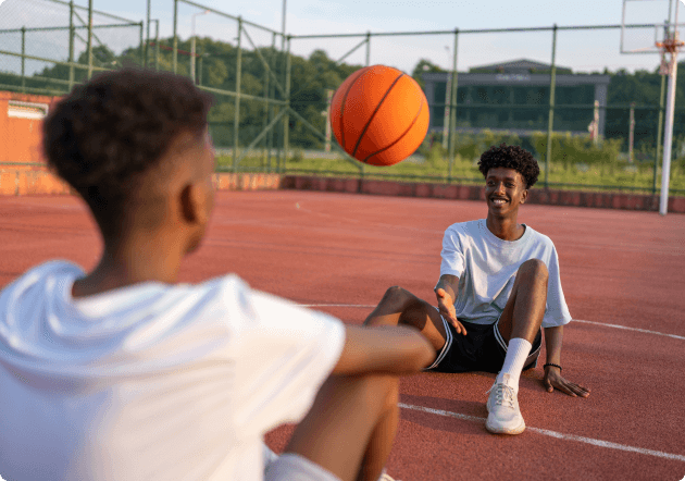 2 donkere jongens zitten op een basketbalveld en spelen de bal over