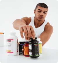 bodybuilder kijkt naar verschillende supplementen die op tafel voor hem staan