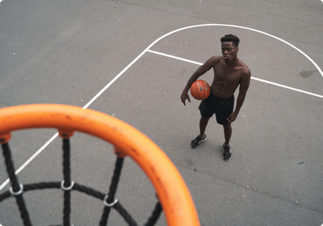 man in ontbloot bovenlijf met basketbal onder zijn arm kijkt naar de basket