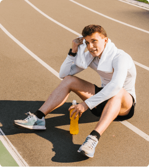 man zit op atletiek baan en veegt zweet van zijn hoofd met een handdoek