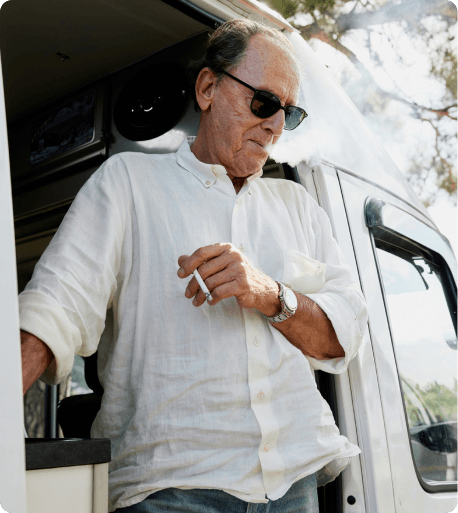 oudere man rookt en staat in de opening van zijn camper