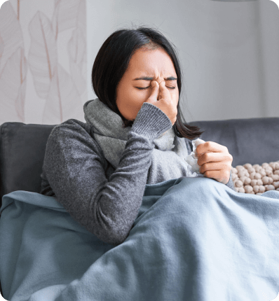 vrouw zit verkouden onder een deken op de bank